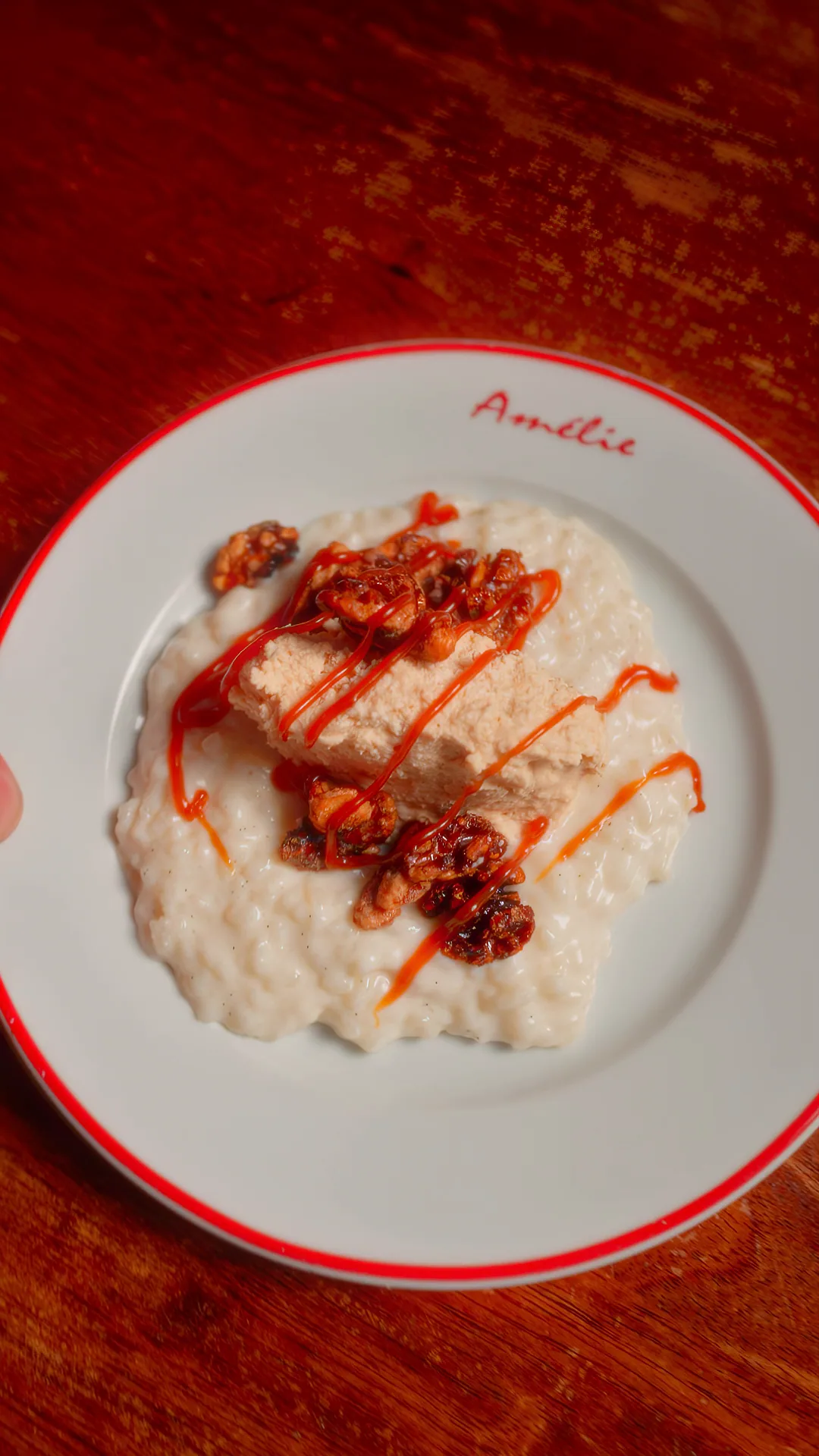 Rice pudding on an Amélie red-rimmed plate, drizzled with red caramel and scattered with praline