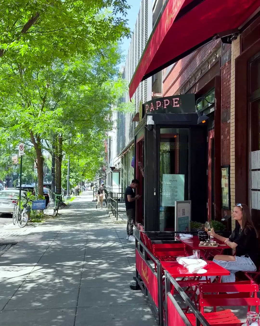 Amélie's red awning over its sidewalk terrace of red bistro tables on a leafy 14th Street in summer