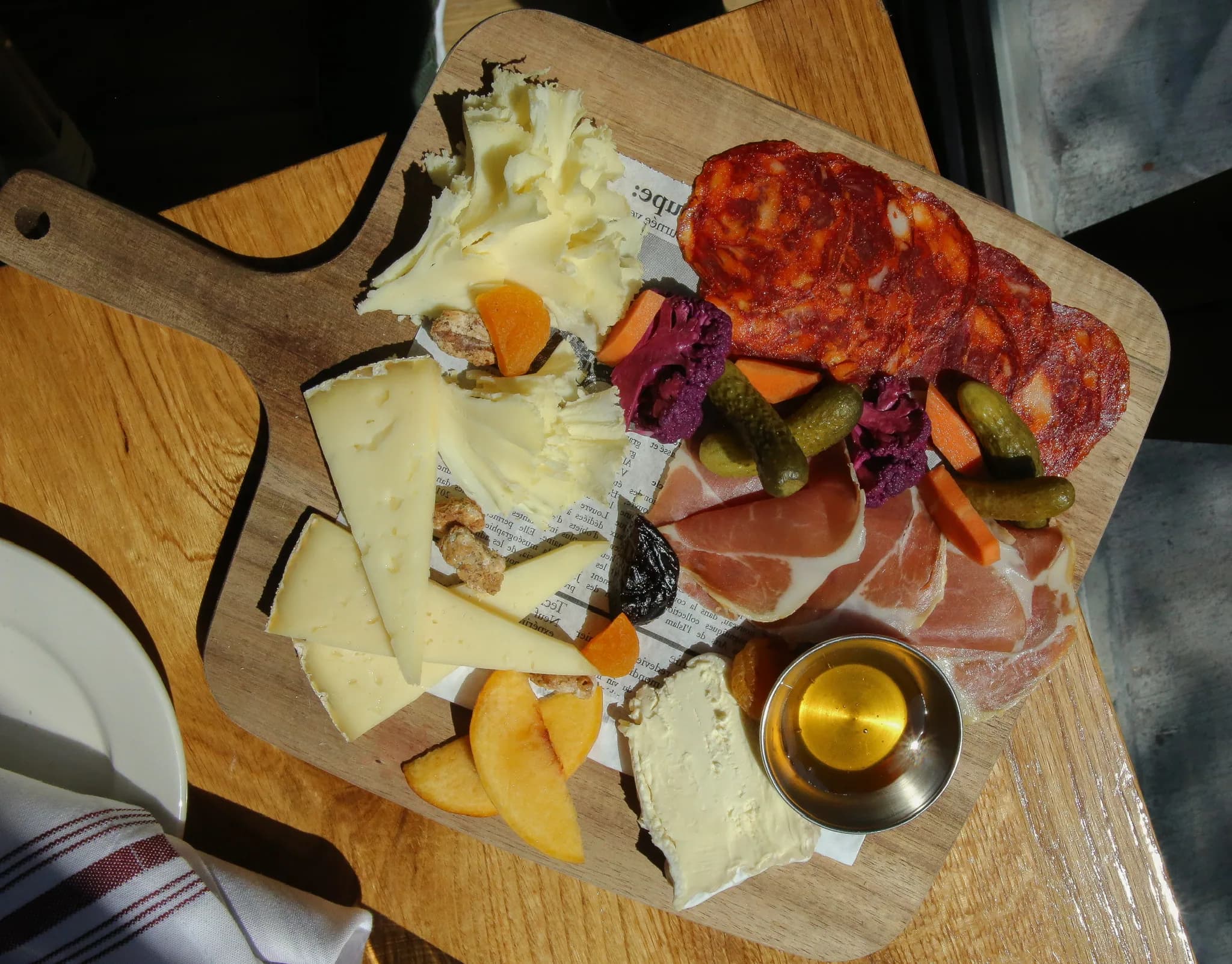 A cheese and charcuterie board with cornichons, honey and cured meats, shot from above on a wooden table