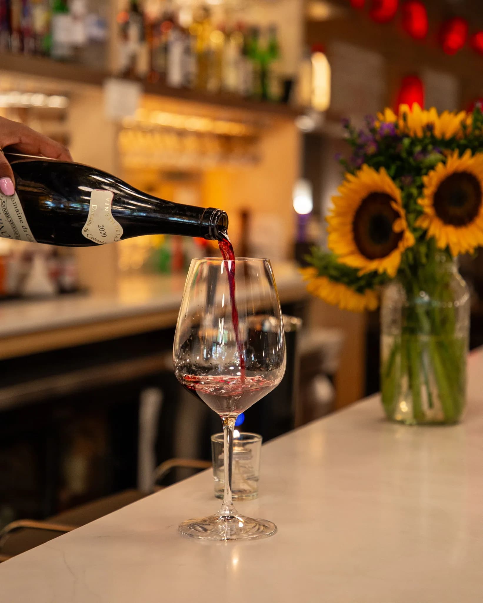 Red wine being poured into a glass on the marble bar at Amélie Washington D.C., sunflowers behind