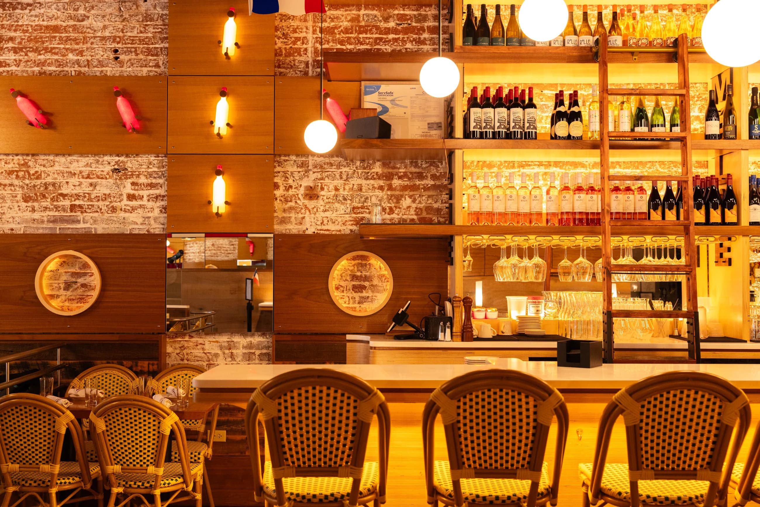 The bar at Amélie Washington D.C., globe pendant lights over exposed brick and a row of woven bistro stools